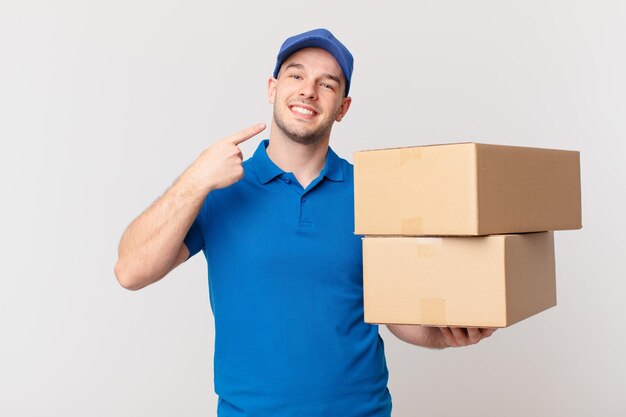 package deliver man smiling confidently pointing to own broad smile, positive, relaxed, satisfied attitude