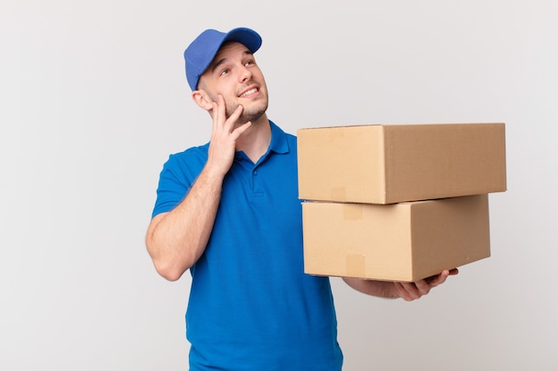 Package deliver man smiling happily and daydreaming or doubting, looking to the side