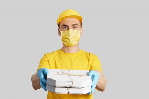 Pacchetto per la porta. il corriere in uniforme gialla, maschera protettiva e guanti offre pizza e caffè da asporto. servizio di consegna in quarantena.