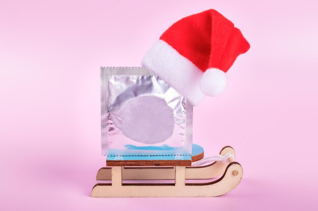 Package with condom and red santa\'s christmas hat on it on pink\
background