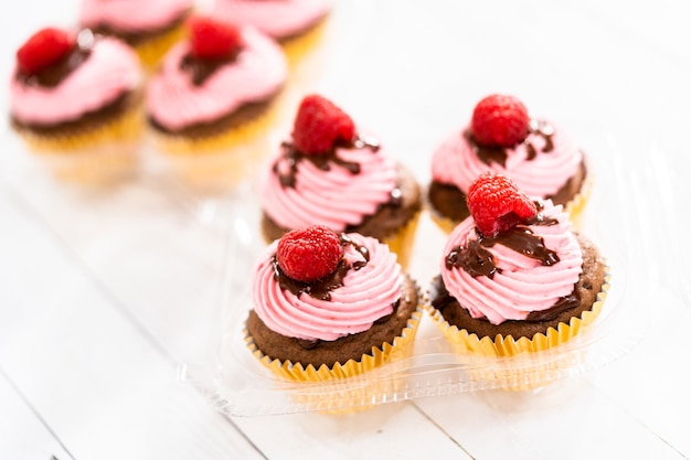 Foto confezionamento di cupcakes al cioccolato e lamponi gourmet in scatole di plastica trasparente.