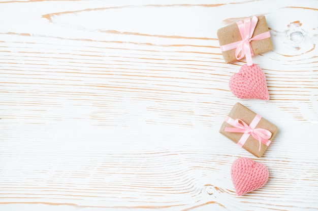 Packed gifts with pink ribbon and knitted hearts on a white wood, top view