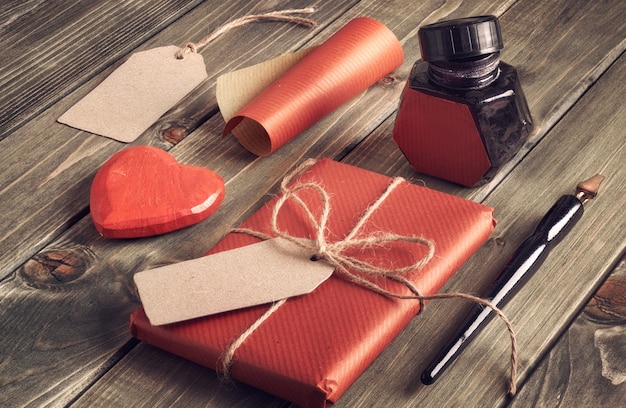 Packed present, wrapping  paper, labels, ink well, pens and decorative heart on wood