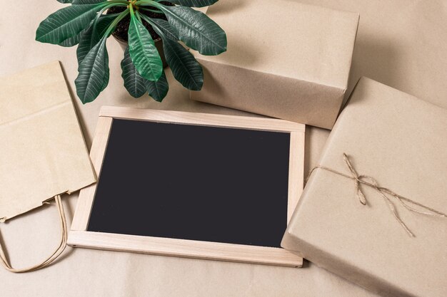 Packing Boxes and Shopping Bag on Grey background with Green Plant and Black shopping board, top view.