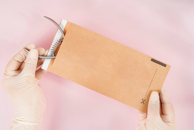 Packing a manicure tool in kraft packages before sterilizing in a dry oven. Manicure tool in the hands of the master isolated on pink background. Close up.