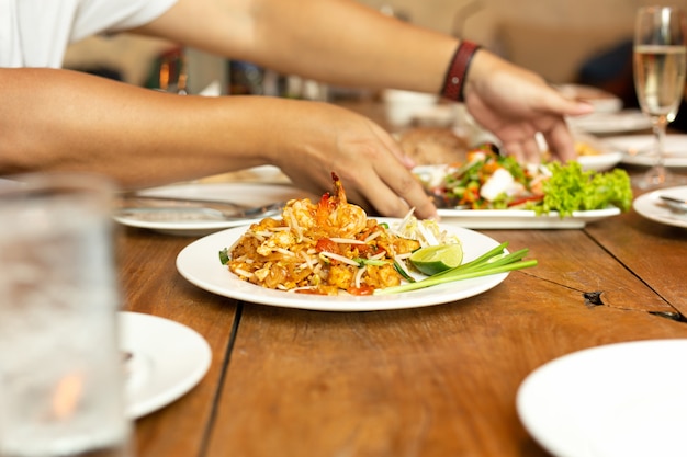 Pad Thai noodles with shrimp on whit plate on wooden table in restaurant.