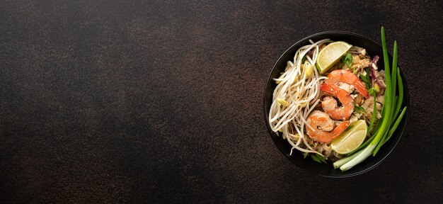 Pad thai thai fried noodles with shrimp and and sprouts on a dark background top view copy space