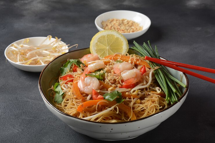 Pad Thai - традиционное тайское блюдо с жареной рисовой лапшой, креветками и овощами на темной поверхности, копией пространства