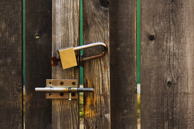 A padlock with a key and a latch on the wooden gate.