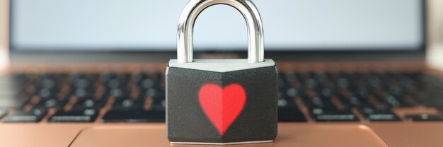 Padlock with painted red heart standing on laptop keyboard closeup