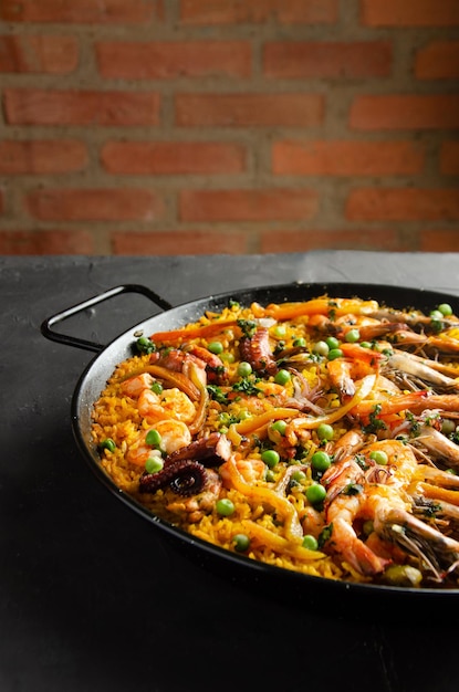 Paella geserveerd in paella pan op zwarte achtergrond en bakstenen muur.