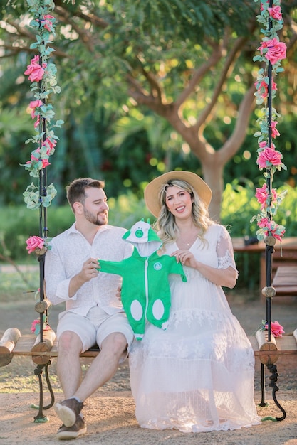 Foto pai e mãe grávida segurando a roupa do bebe no balanço