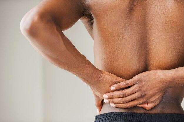 Pain in back. Cropped image of young African man touching his back