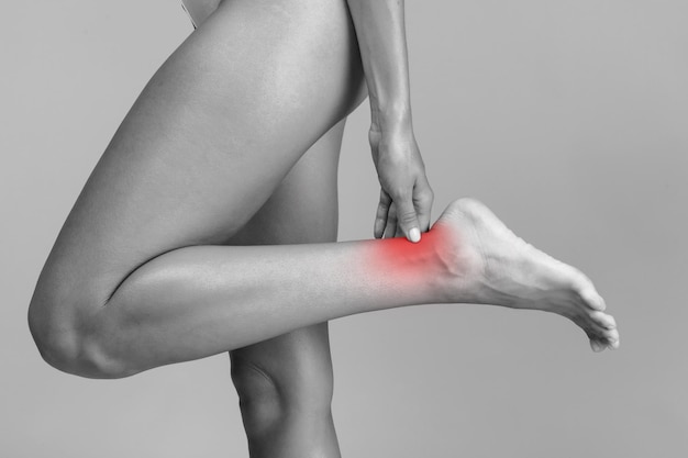 Фото Женщина с болью в ногах, страдающая от боли, черно-белое фото с красным пятном, указывающим на место травмы