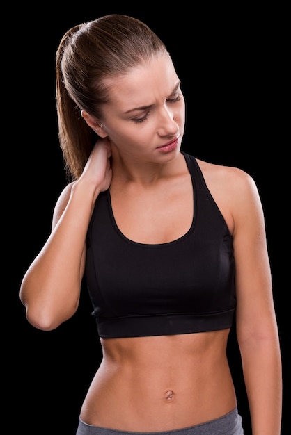 Pain in muscles. Frustrated young woman touching her neck and keeping eyes closed  while standing against black background