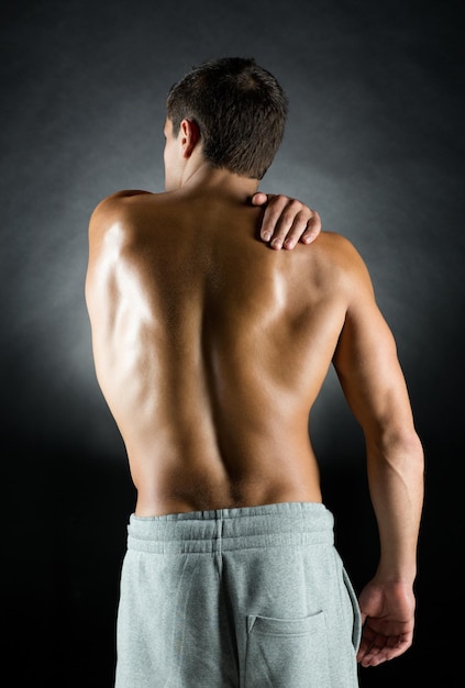 pain relief, sport, bodybuilding, strength and people concept - young man standing over black background