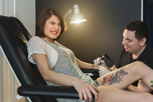 Painful tattooing process, young woman grimacing while master making tattoo on her arm. Popular body modification, modern lifestyle, copy space