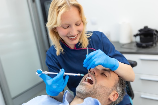 Iniezione di anestesia antidolorifico dentista che esamina i denti di un paziente in un moderno studio di odontoiatria primo piano immagine ritagliata con copyspace dottoressa in uniforme blu