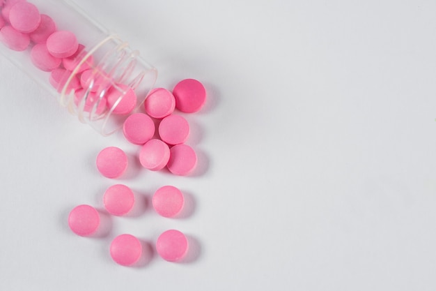 Painkillers pink pills from a transparent plastic jar are scattered on white