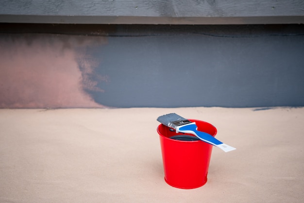 Paint brush and a bucket with paint next to a building wall.