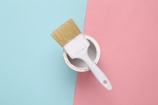 Paint brush and can of white paint on pink blue background top view home renovation concept