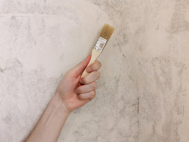 Paint brush in hand Beige background Repair in the apartment Place for text