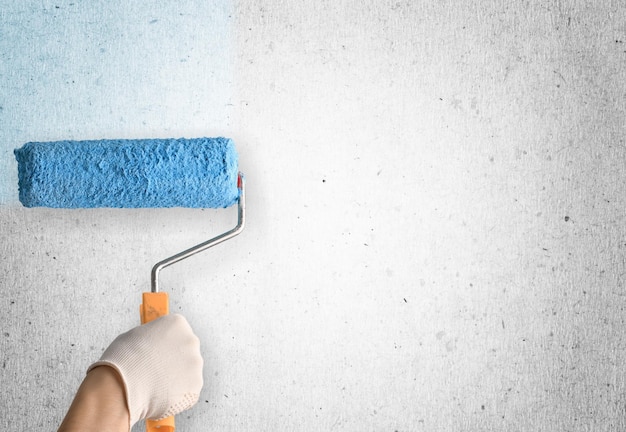 Paint brush or paint roller in a hand painter worker painting on surface wall