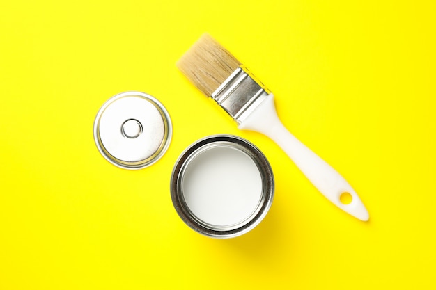 Paint can and brush on yellow surface