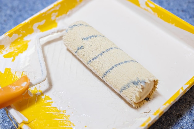 The paint roller is in a yellow tray with beige paint the\
concept of repair and painting of premises closeup