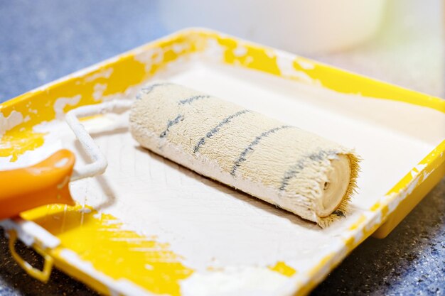 The paint roller is in a yellow tray with beige paint the
concept of repair and painting of premises closeup