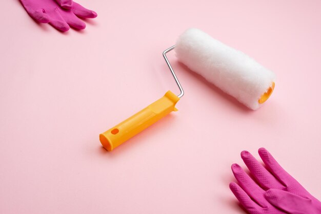 paint roller and latex gloves lying on diagonal on pink background