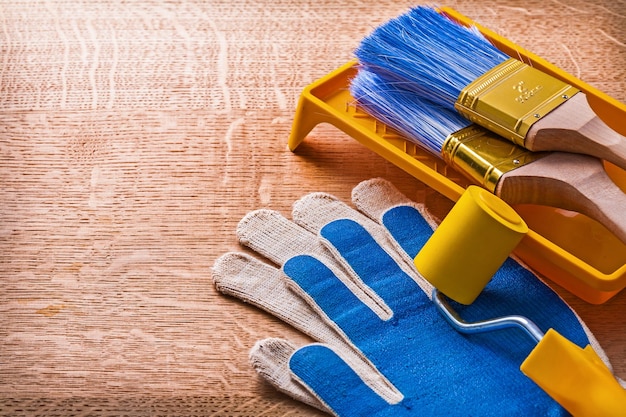 Paint roller tray brushes and protective gloves on wooden board construction concept