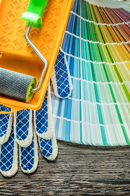 Paint roller tray protective gloves color palette on wooden board.