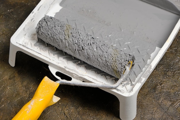 Paint roller with yellow handle in tray for roller with gray paint on concrete floor