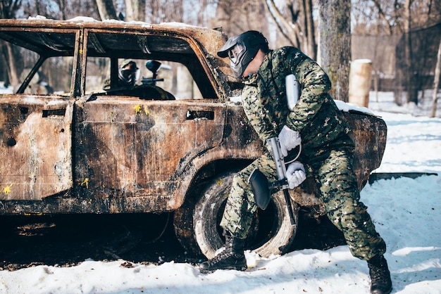 Пейнтбольный бой вокруг сгоревшей машины в зимнем лесу, пейнтбол. Экстремальный спорт, военная игра