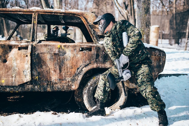 Paintballgevecht rond verbrande auto in winterbos, paintball. Extreme sport, militair spel