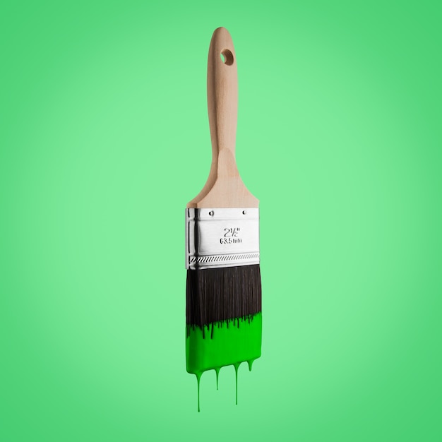 Paintbrush loaded with green color dripping off the bristles- Isolated on green background.