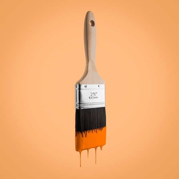 Paintbrush loaded with orange color dripping off the bristles- Isolated on orange background.