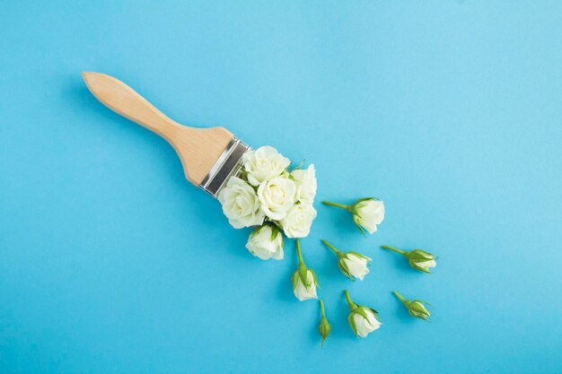 Paintbrush with white roses on the blue background Top view Copy space