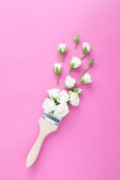 Paintbrush with white roses on the pink background Top view Location vertical