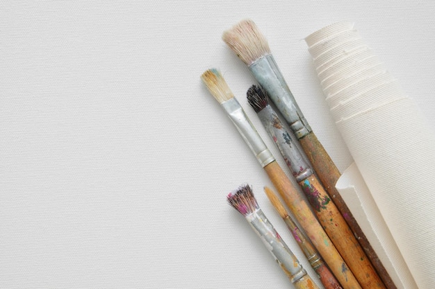 Paintbrushes and roll of artist canvas on white canvas background Top view Copy space for text