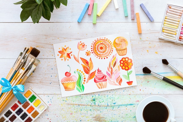 Paintbrushes with watercolors and blank mock up paper on white wooden table