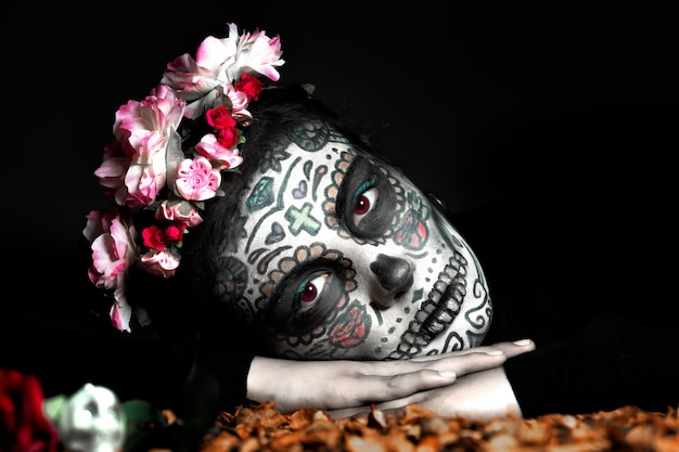 Painted Catrina woman leaning on her hands looking at camera on black background, day of the dead, halloween.