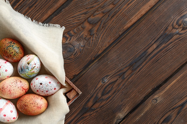 Painted colored Easter eggs on canvas in dark wooden box on wooden background