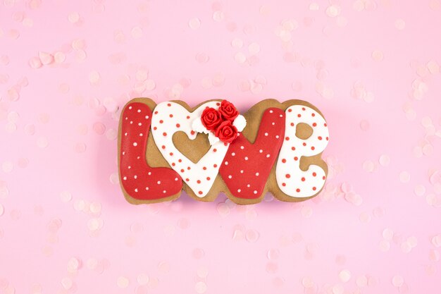 Painted gingerbread cookies in shape of word love on a pink desk. Love romance concept.Top view. Copy space