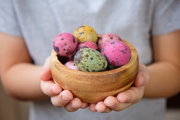 Painted quail eggs in a bowl in child's hands for Easter