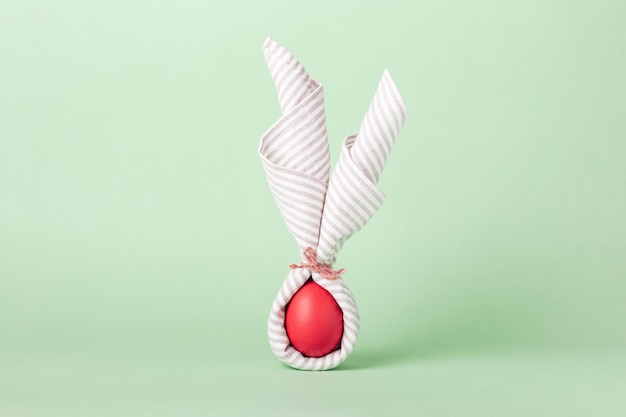 Uovo di pasqua dipinto di rosso decorato con un tovagliolo a forma di coniglietto su sfondo verde