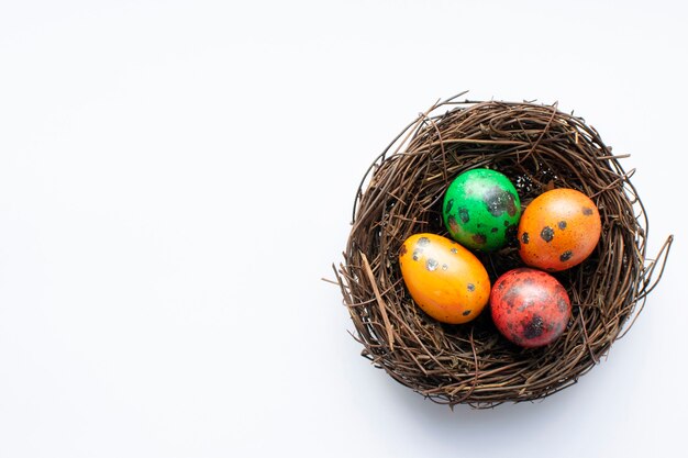 Painted red, orange, yellow, green quail eggs in a decorative nest of twigs on a white surface