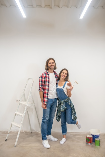 Painted wall. Young couple standing near the white wall