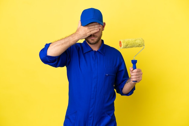 Painter Brazilian man isolated on yellow background covering eyes by hands. Do not want to see something